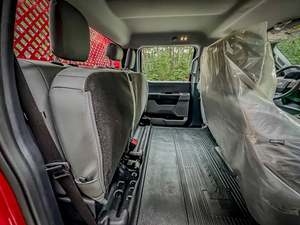 Rear cabin view with rear bench and front seatback covered in plastic.