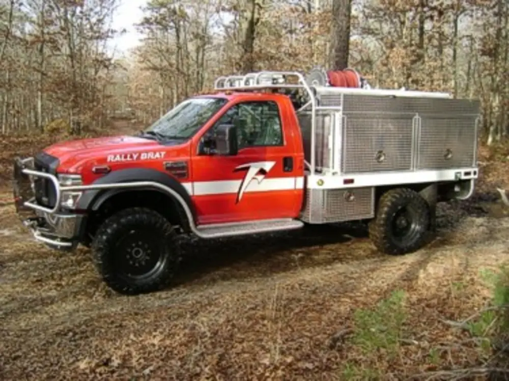 Exterior view of small fire truck showing cab, body compartments, and wheel/tire area.