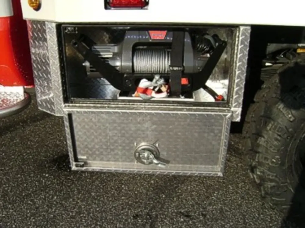 Exterior view of small fire truck showing cab, body compartments, and wheel/tire area.