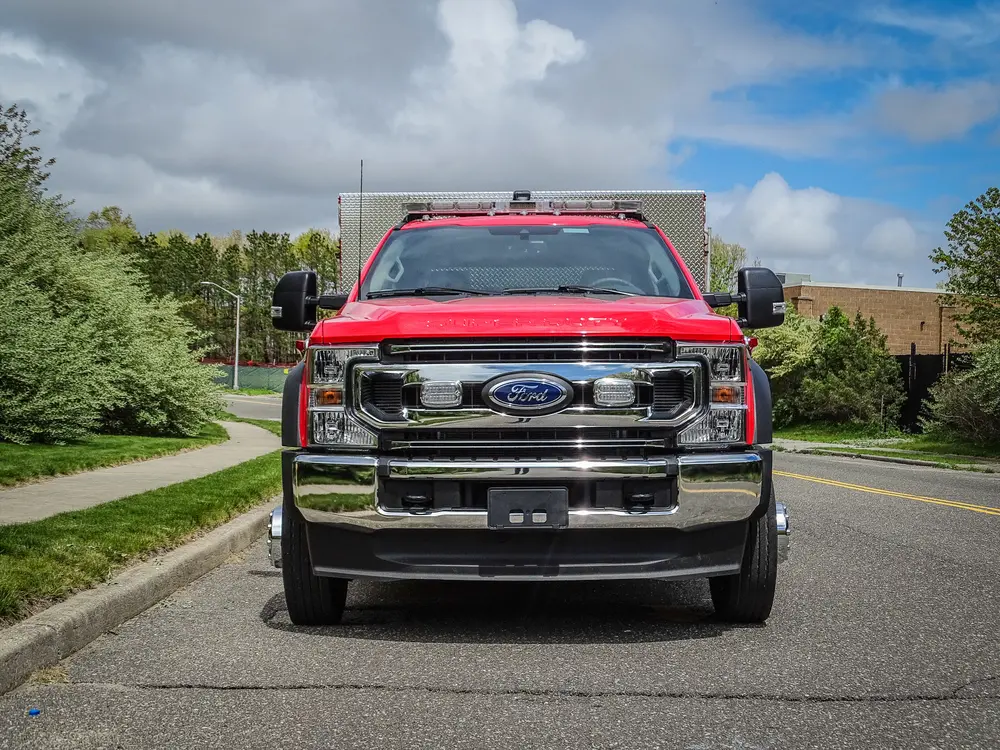 Exterior view of small fire truck showing cab, body compartments, and wheel/tire area.