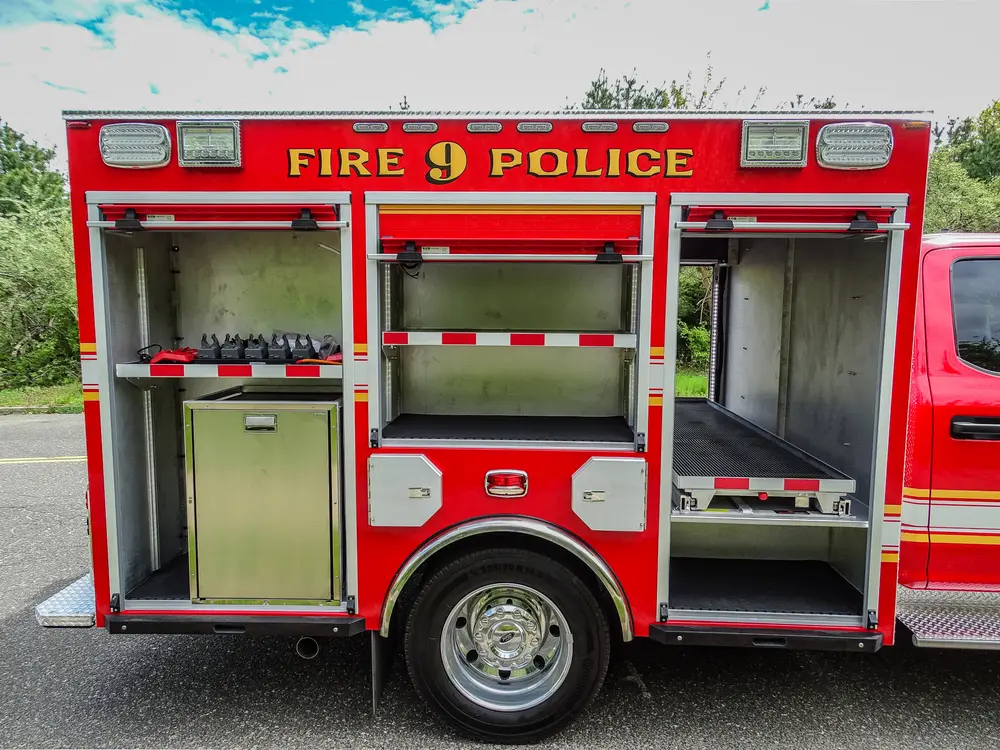 Exterior view of small fire truck showing cab, body compartments, and wheel/tire area.