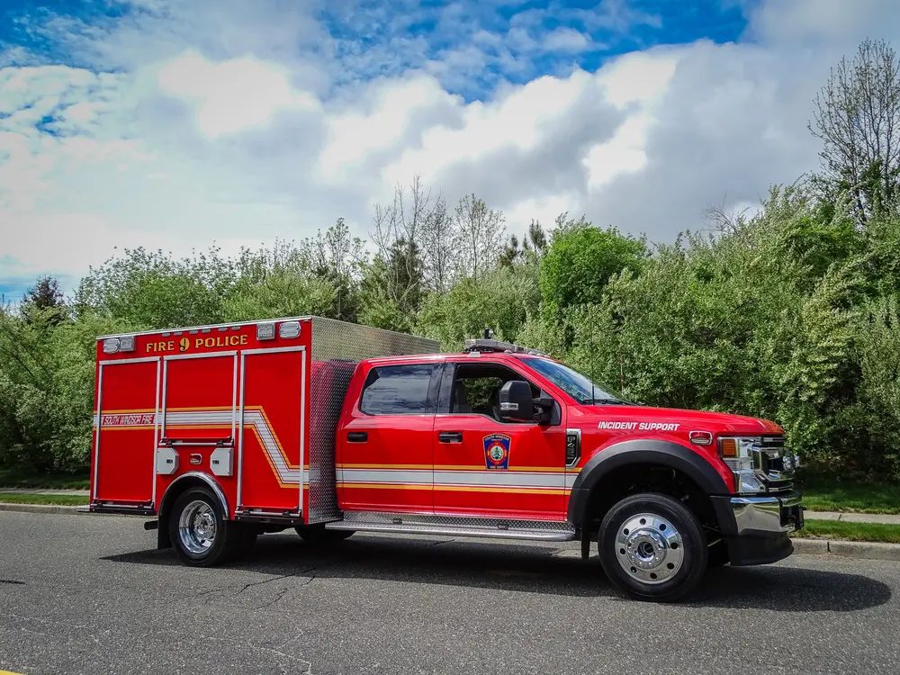 Exterior view of small fire truck showing cab, body compartments, and wheel/tire area.