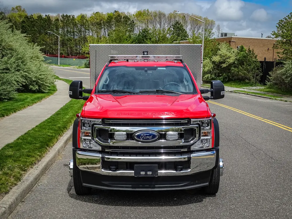 Exterior view of small fire truck showing cab, body compartments, and wheel/tire area.