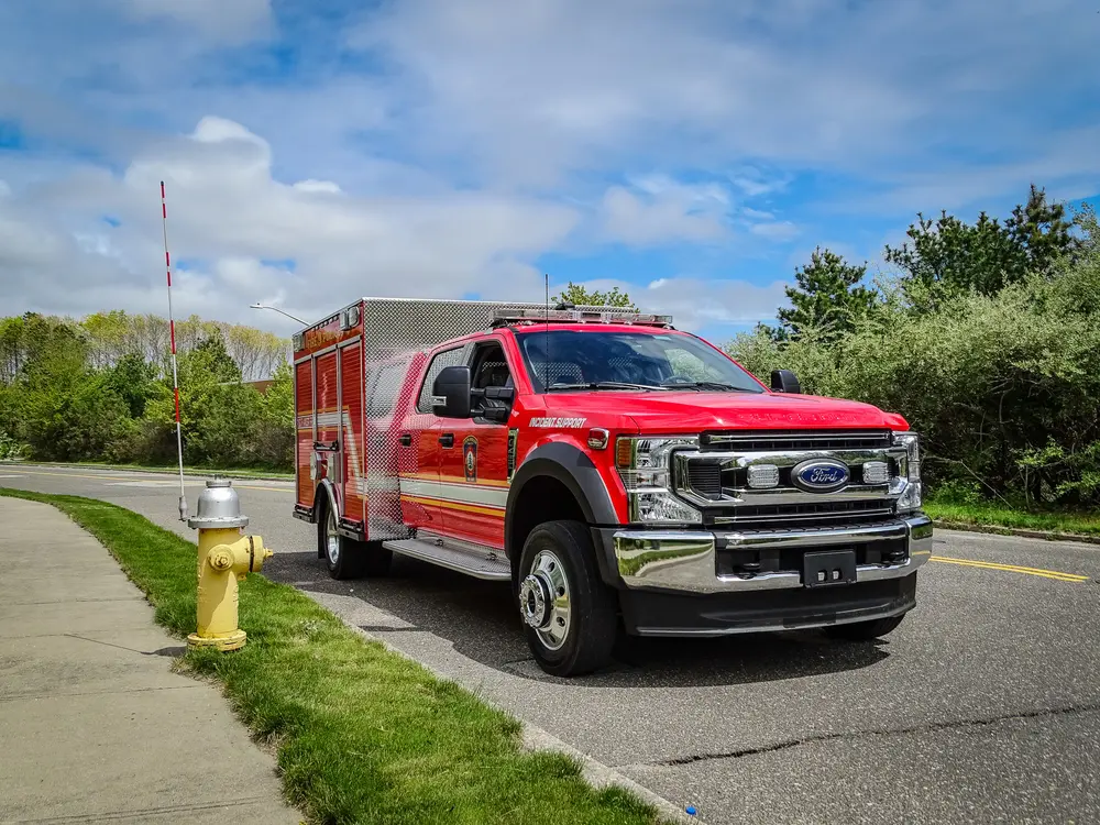 Exterior view of small fire truck showing cab, body compartments, and wheel/tire area.