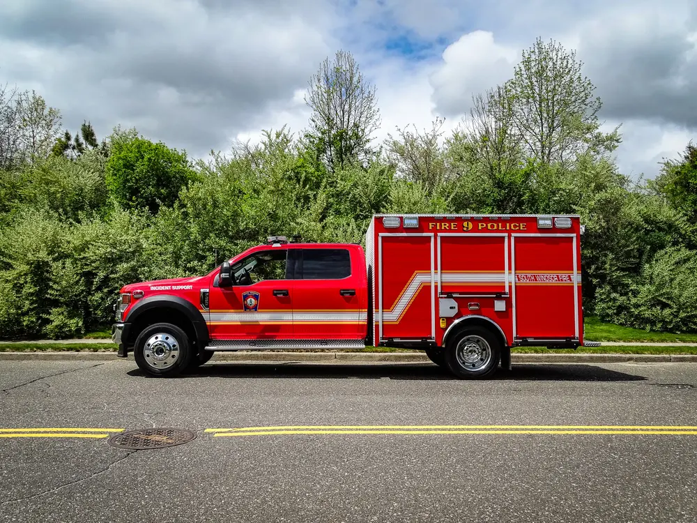 Exterior view of small fire truck showing cab, body compartments, and wheel/tire area.