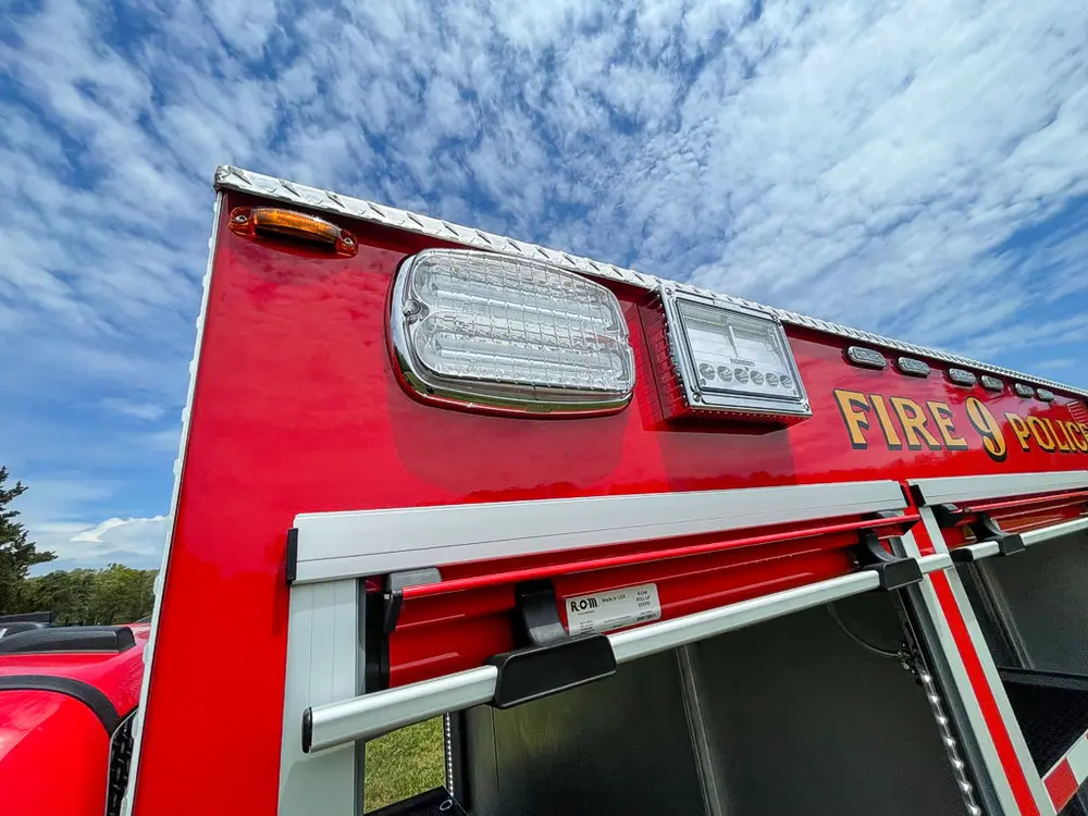 Exterior view of small fire truck showing cab, body compartments, and wheel/tire area.