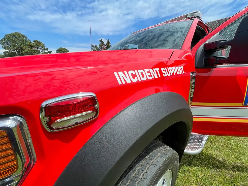 Exterior view of small fire truck showing cab, body compartments, and wheel/tire area.