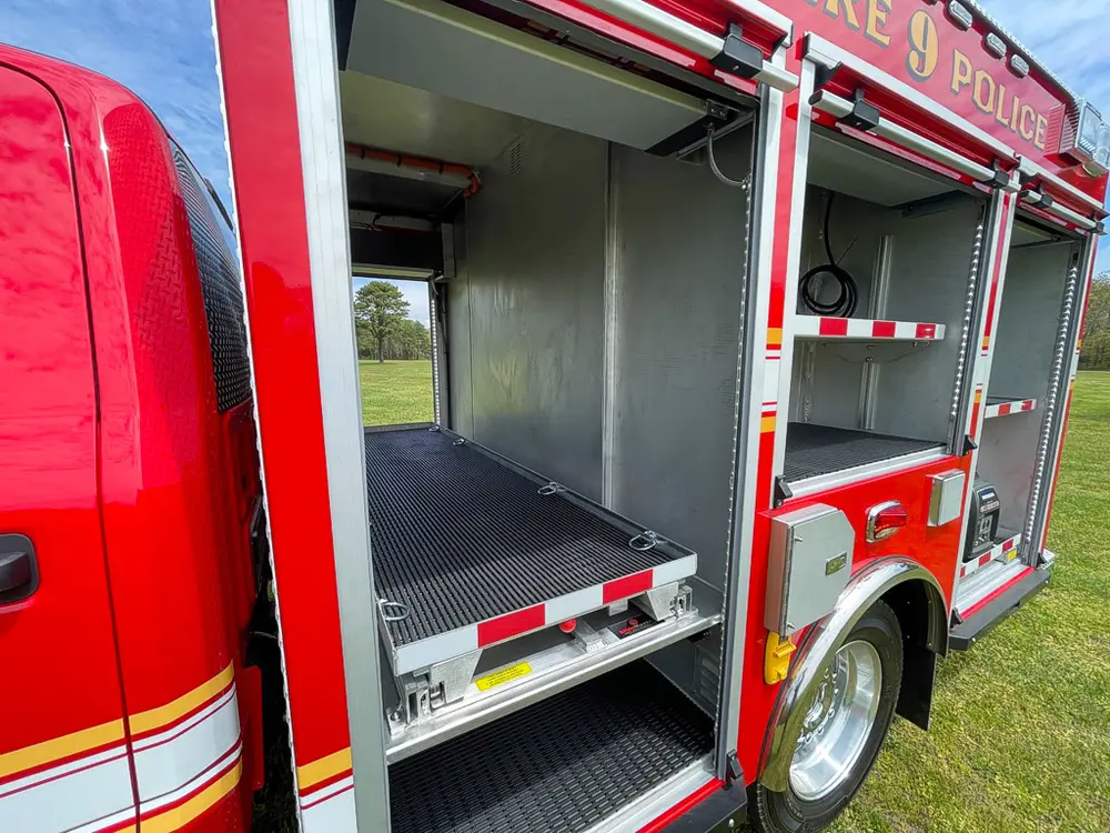 Exterior view of small fire truck showing cab, body compartments, and wheel/tire area.