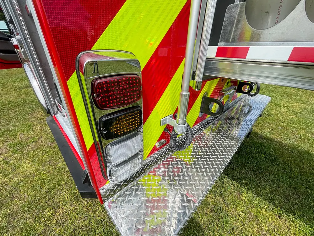 Exterior view of small fire truck showing cab, body compartments, and wheel/tire area.