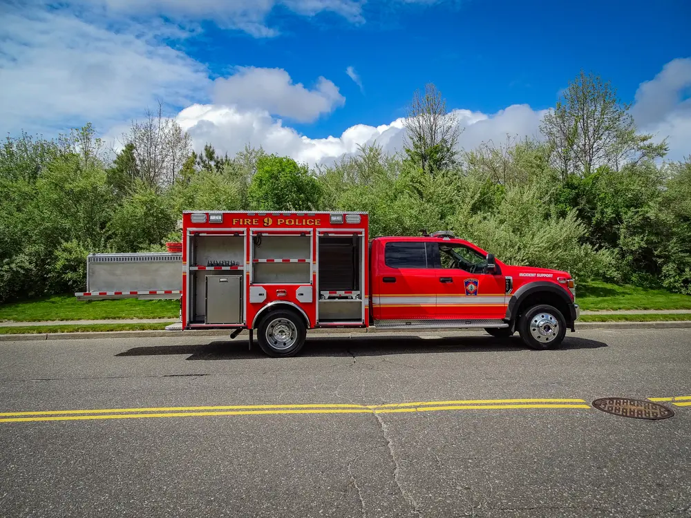 Exterior view of small fire truck showing cab, body compartments, and wheel/tire area.