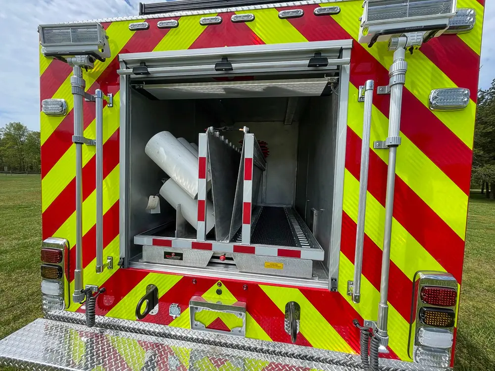 Exterior view of small fire truck showing cab, body compartments, and wheel/tire area.