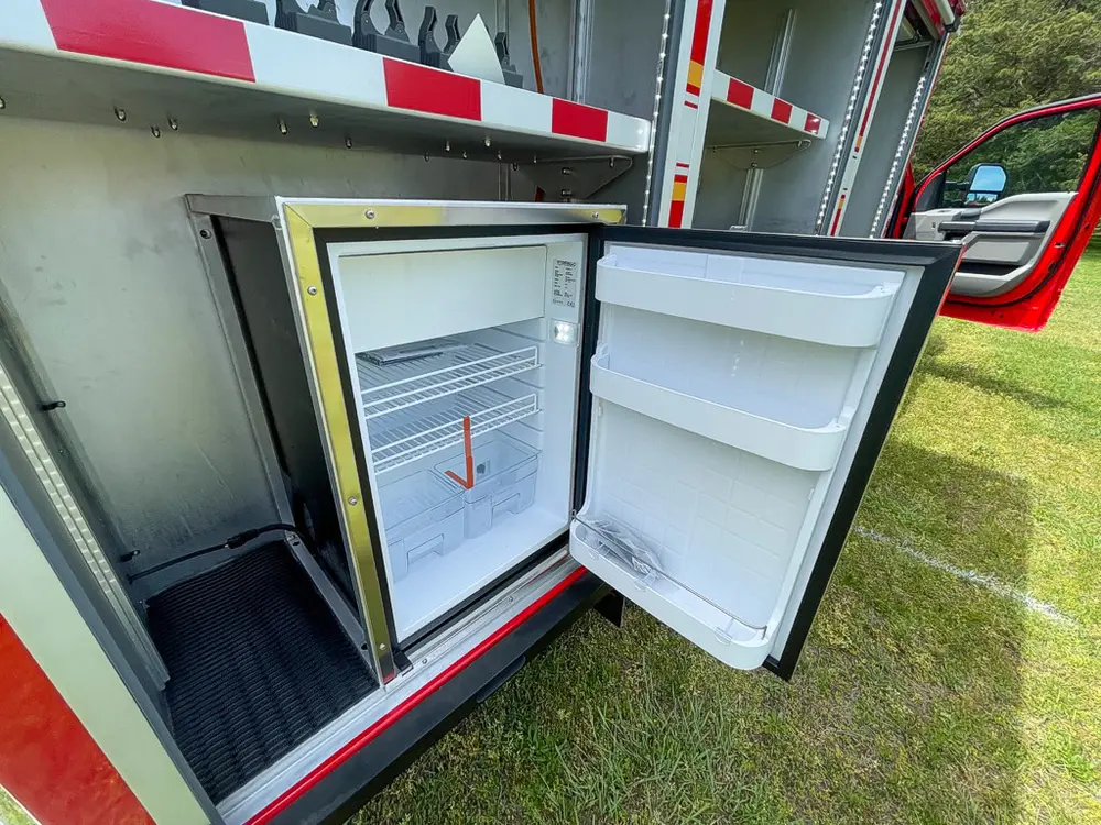 Exterior view of small fire truck showing cab, body compartments, and wheel/tire area.