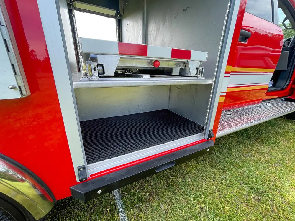Exterior view of small fire truck showing cab, body compartments, and wheel/tire area.