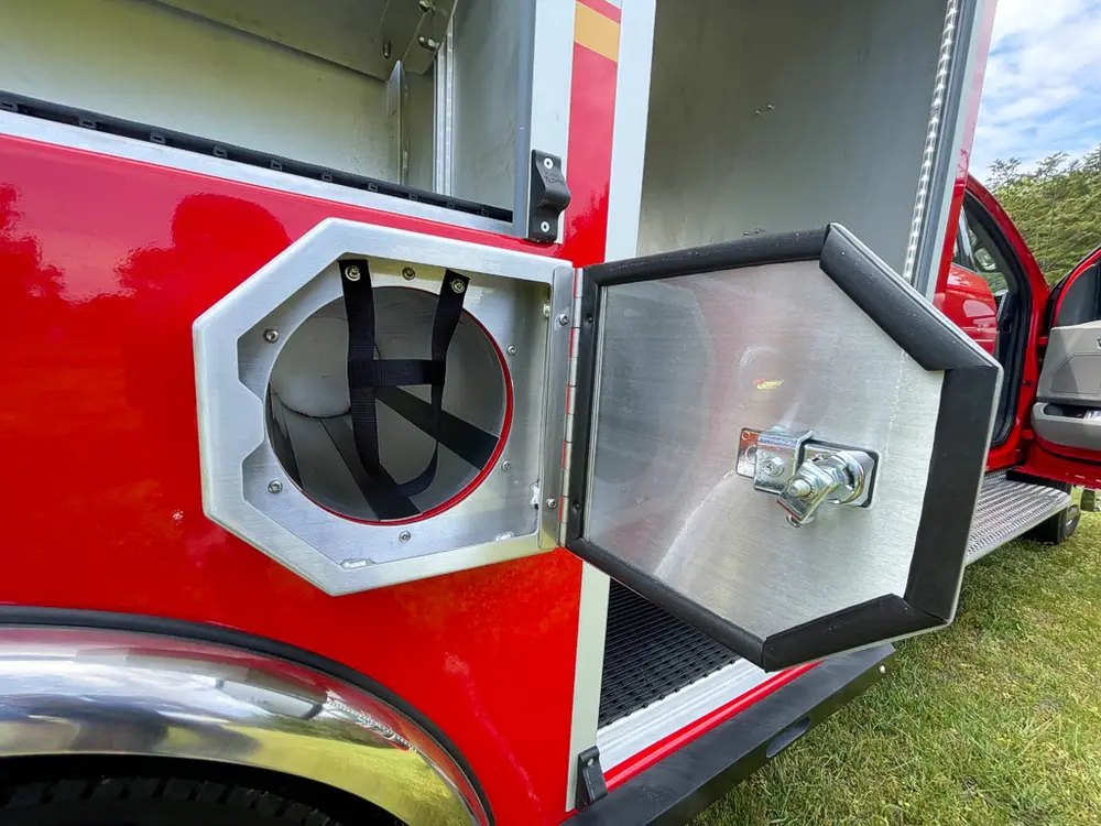 Exterior view of small fire truck showing cab, body compartments, and wheel/tire area.