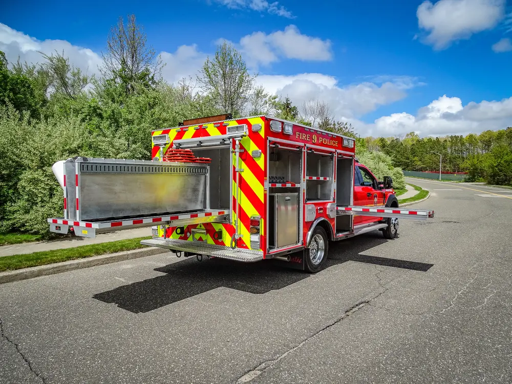 Exterior view of small fire truck showing cab, body compartments, and wheel/tire area.