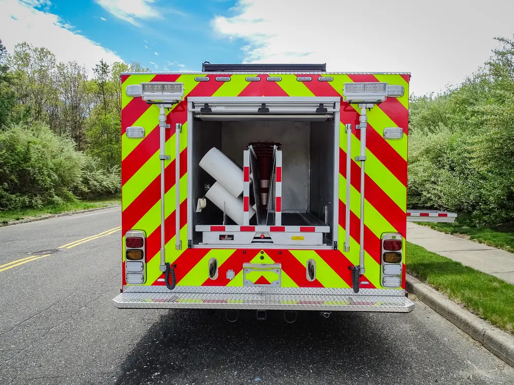 Exterior view of small fire truck showing cab, body compartments, and wheel/tire area.