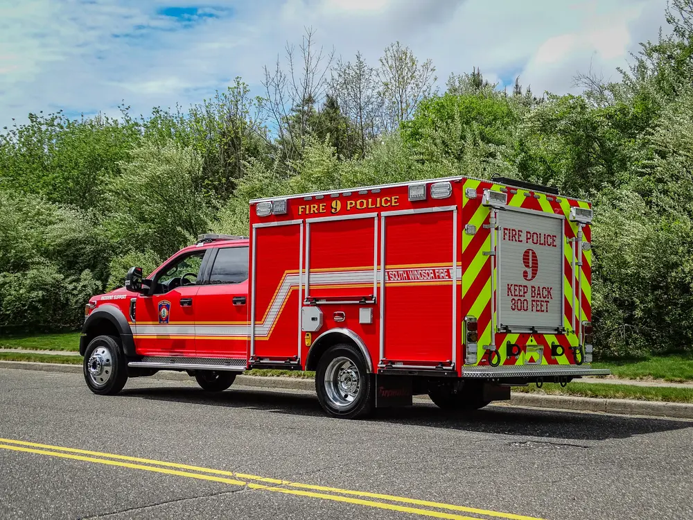 Exterior view of small fire truck showing cab, body compartments, and wheel/tire area.