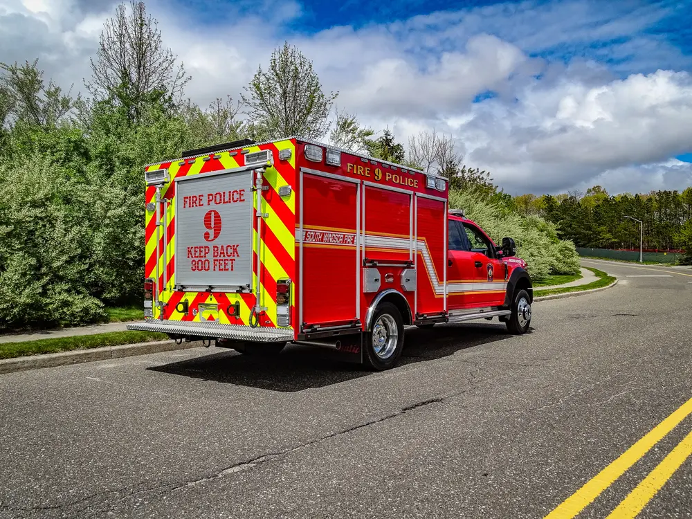 Exterior view of small fire truck showing cab, body compartments, and wheel/tire area.