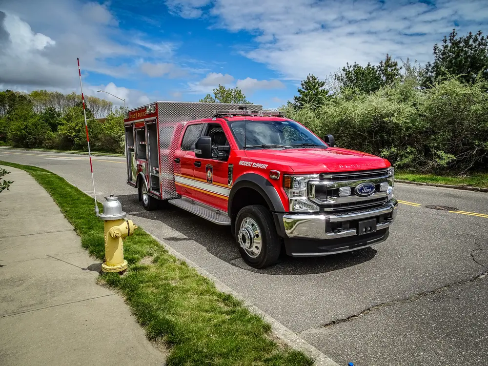 Exterior view of small fire truck showing cab, body compartments, and wheel/tire area.