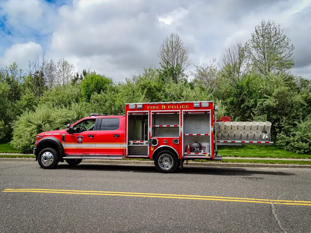 Exterior view of small fire truck showing cab, body compartments, and wheel/tire area.