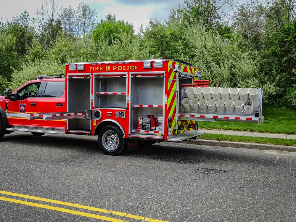 Exterior view of small fire truck showing cab, body compartments, and wheel/tire area.