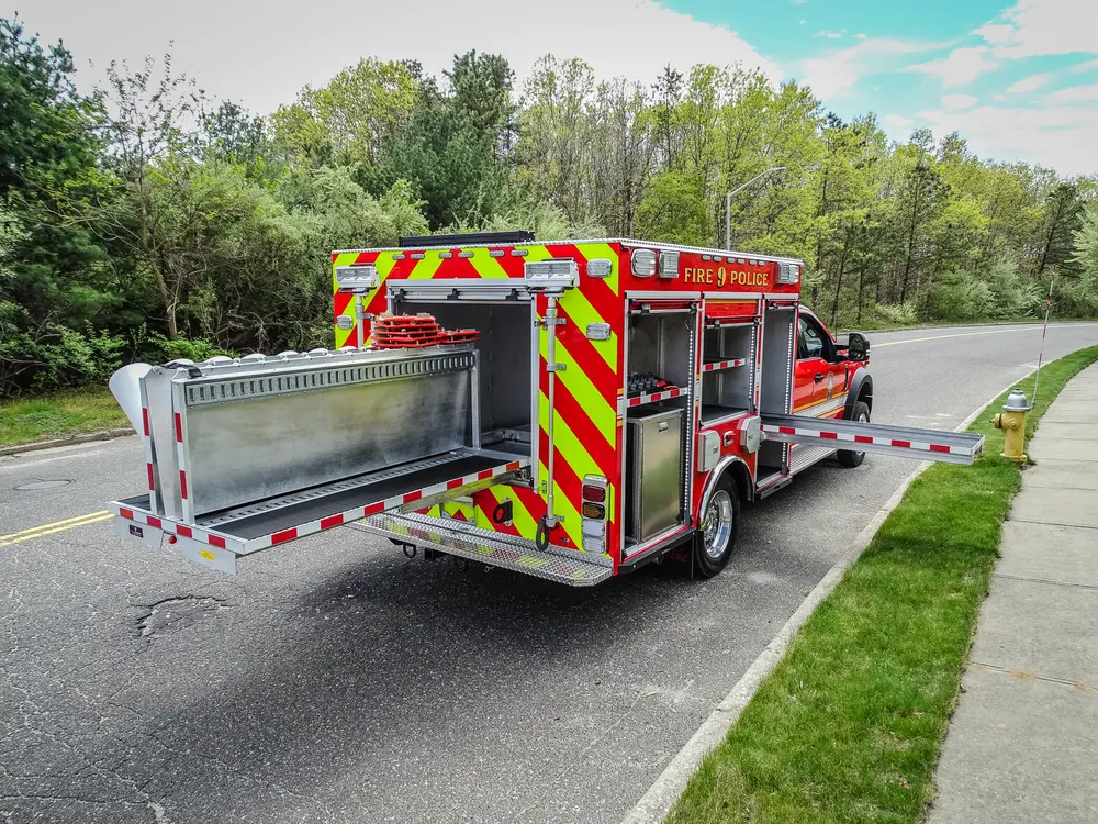 Exterior view of small fire truck showing cab, body compartments, and wheel/tire area.