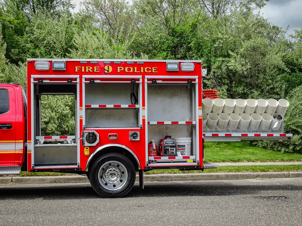 Exterior view of small fire truck showing cab, body compartments, and wheel/tire area.