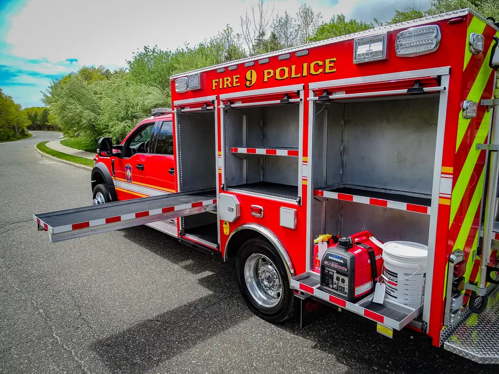 Exterior view of small fire truck showing cab, body compartments, and wheel/tire area.