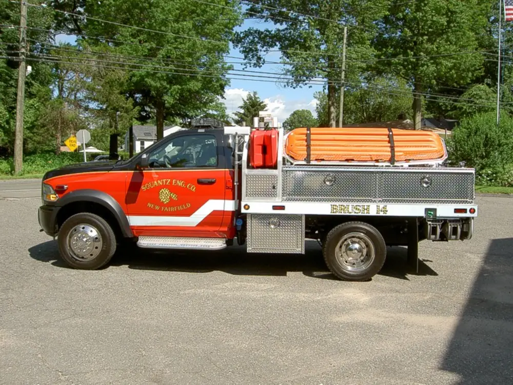Exterior view of small fire truck showing cab, body compartments, and wheel/tire area.