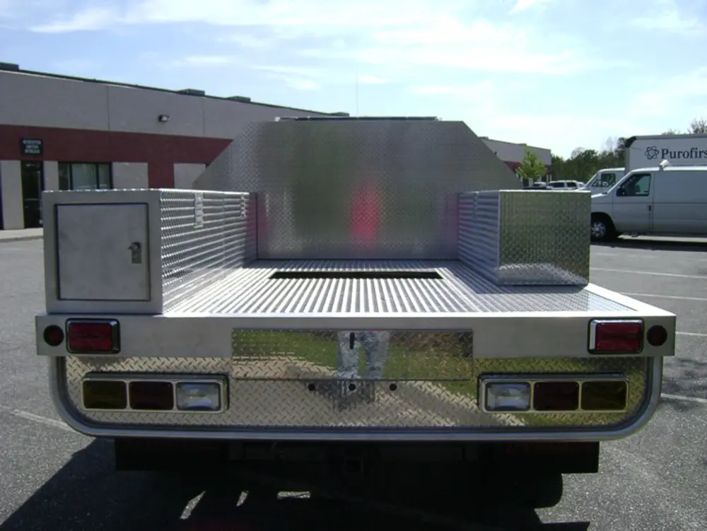 Exterior view of small fire truck showing cab, body compartments, and wheel/tire area.