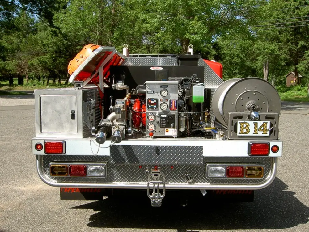 Exterior view of small fire truck showing cab, body compartments, and wheel/tire area.