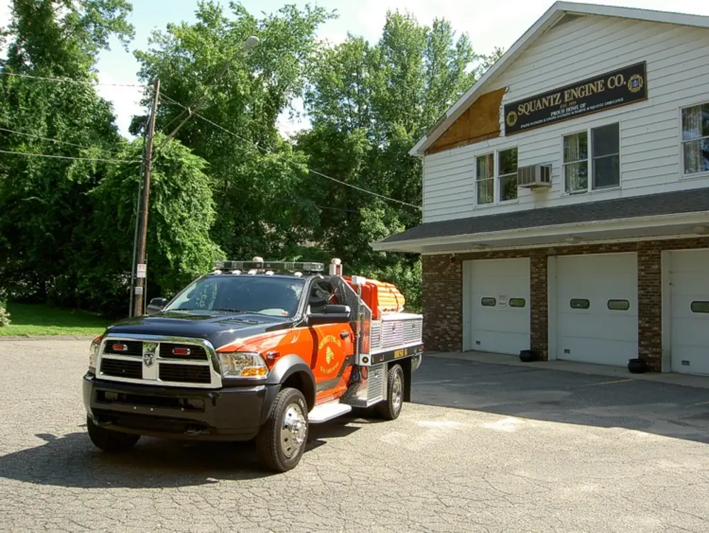 Exterior view of small fire truck showing cab, body compartments, and wheel/tire area.