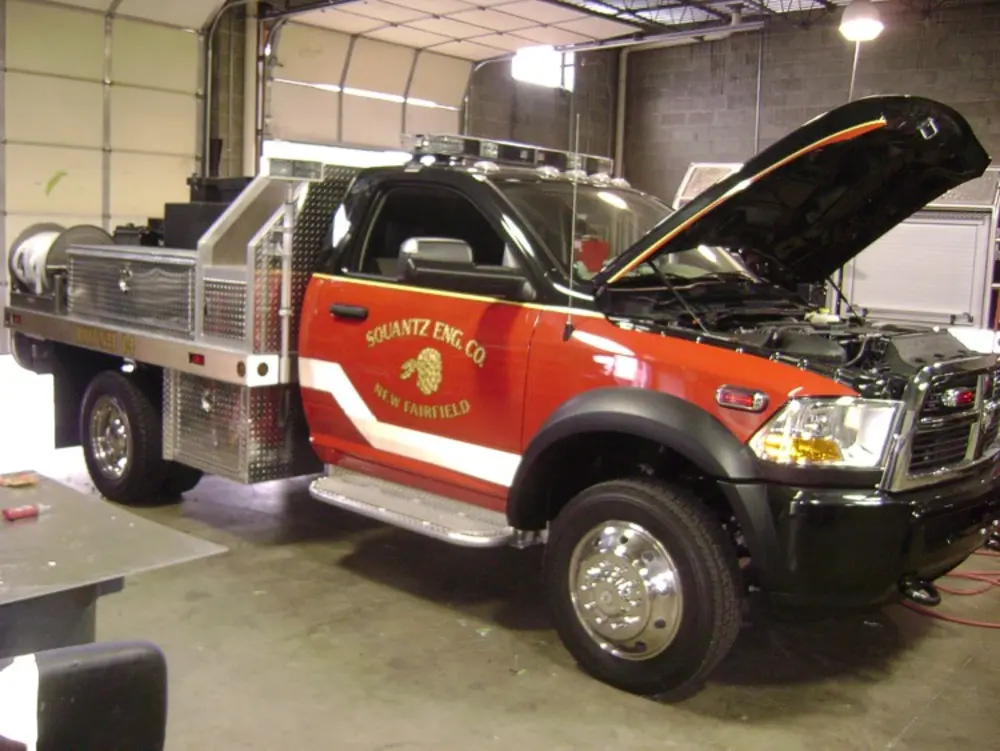 Exterior view of small fire truck showing cab, body compartments, and wheel/tire area.