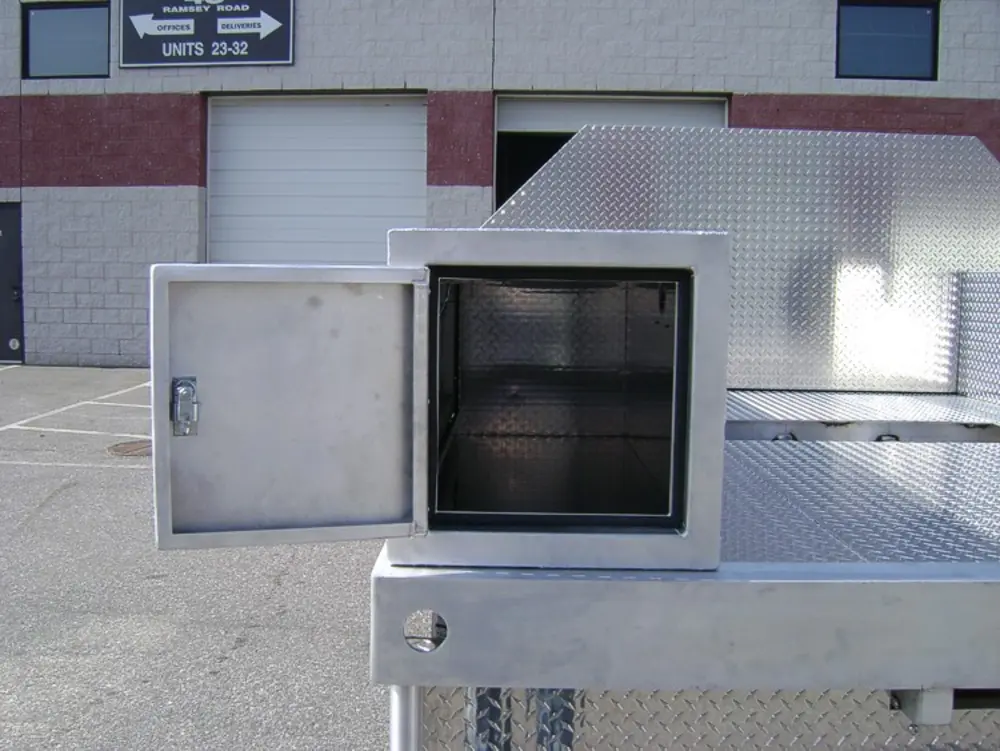 Exterior view of small fire truck showing cab, body compartments, and wheel/tire area.