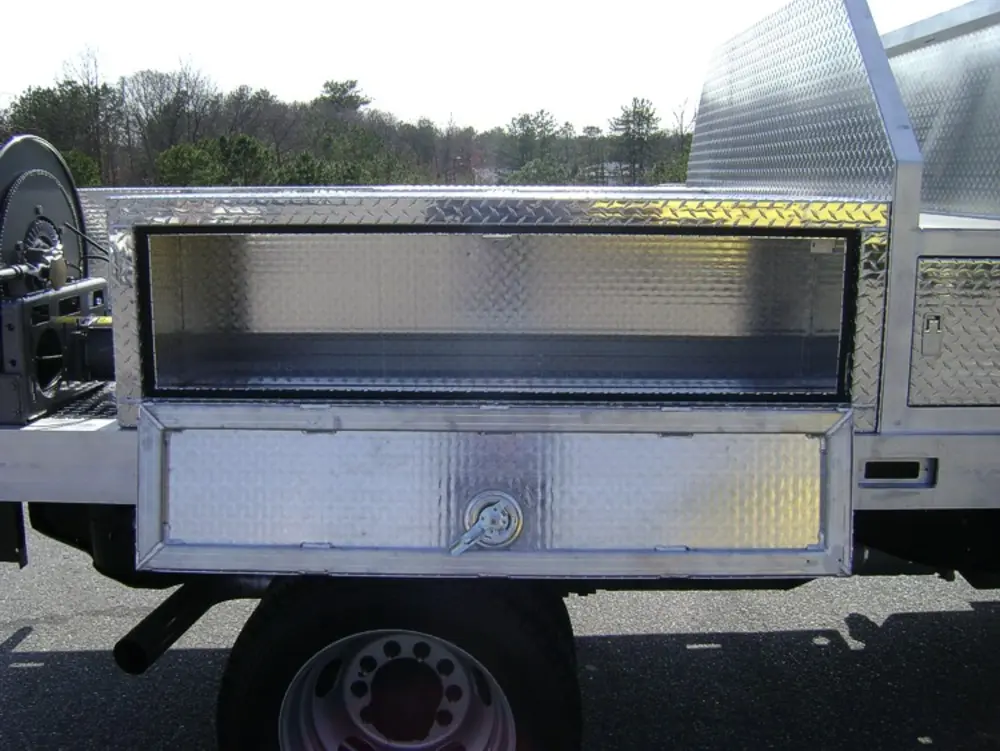 Exterior view of small fire truck showing cab, body compartments, and wheel/tire area.