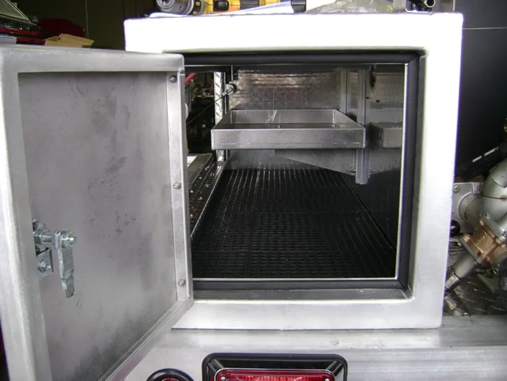 Exterior view of small fire truck showing cab, body compartments, and wheel/tire area.