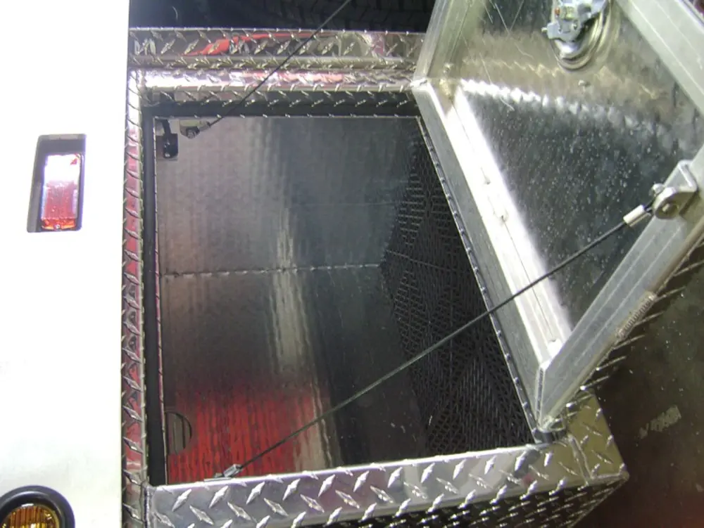 Exterior view of small fire truck showing cab, body compartments, and wheel/tire area.