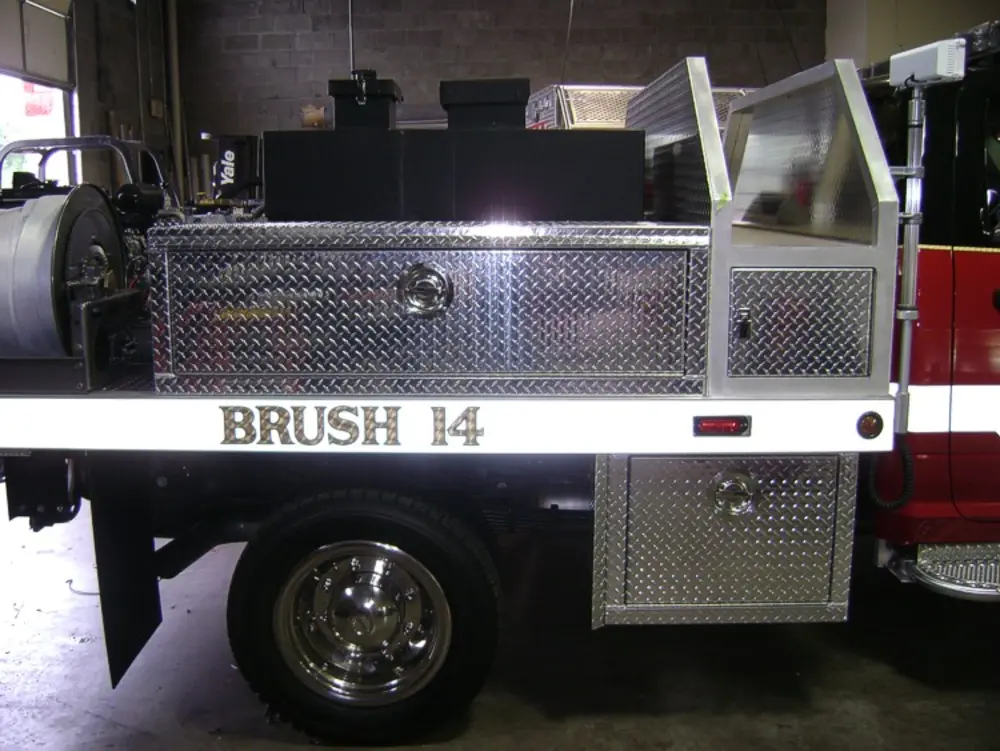 Exterior view of small fire truck showing cab, body compartments, and wheel/tire area.