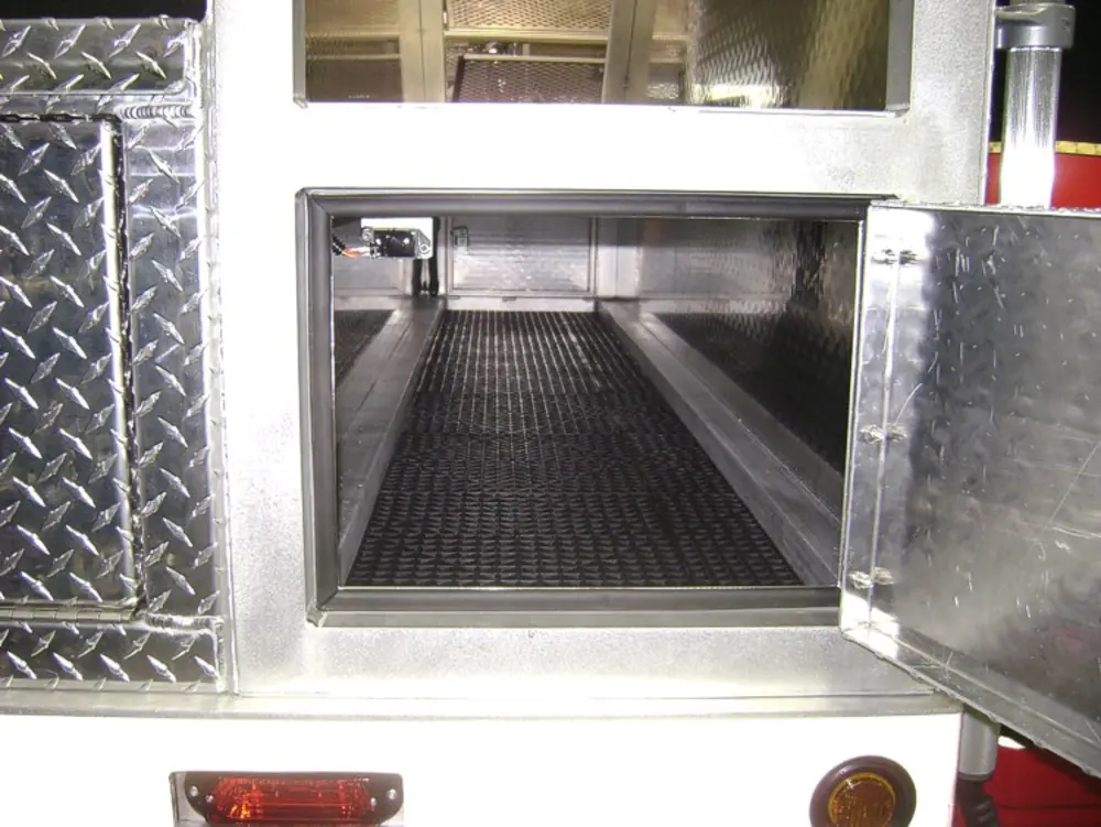 Exterior view of small fire truck showing cab, body compartments, and wheel/tire area.