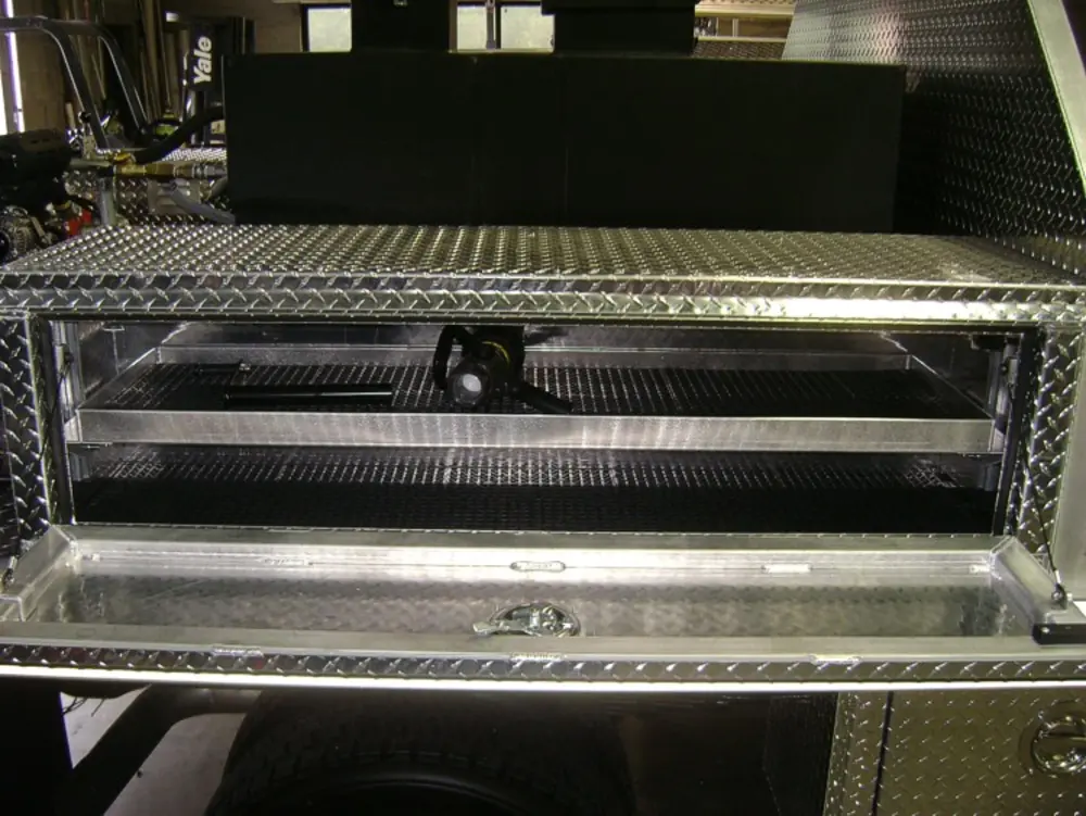 Exterior view of small fire truck showing cab, body compartments, and wheel/tire area.