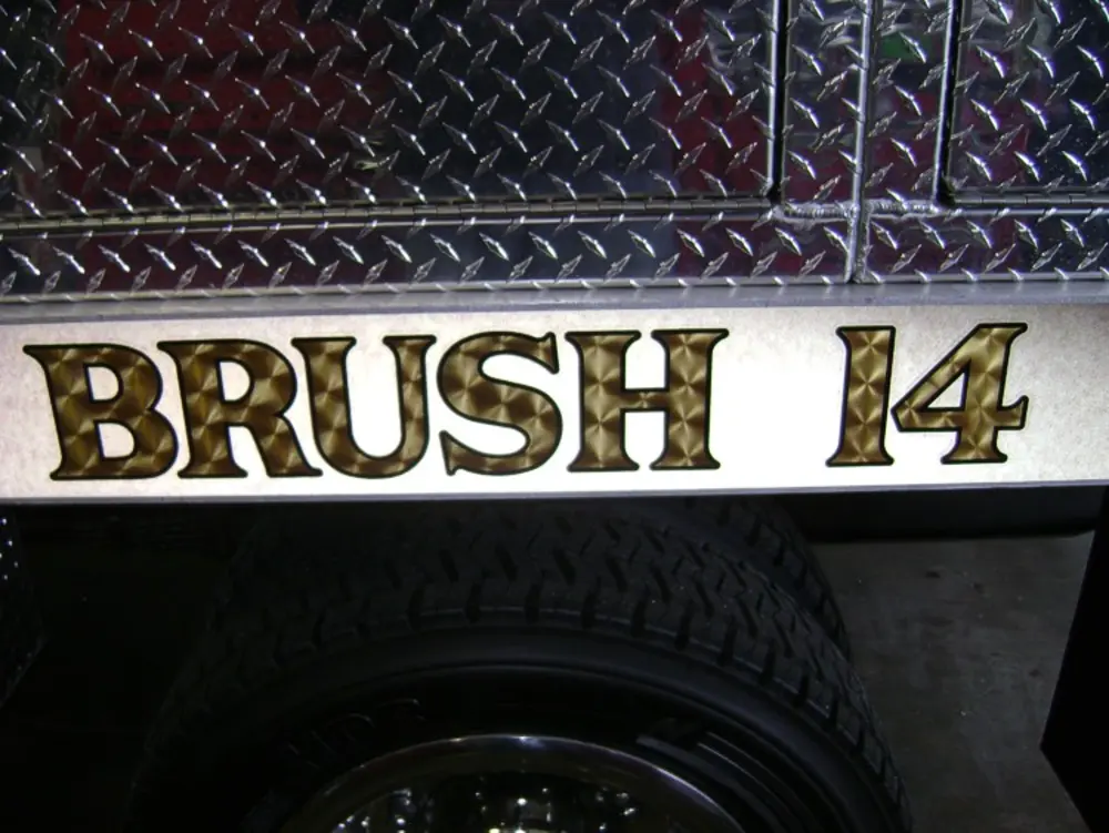 Exterior view of small fire truck showing cab, body compartments, and wheel/tire area.