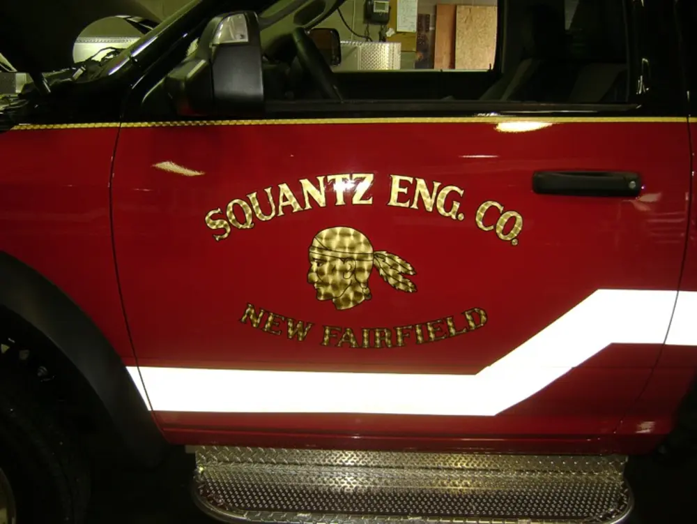 Exterior view of small fire truck showing cab, body compartments, and wheel/tire area.