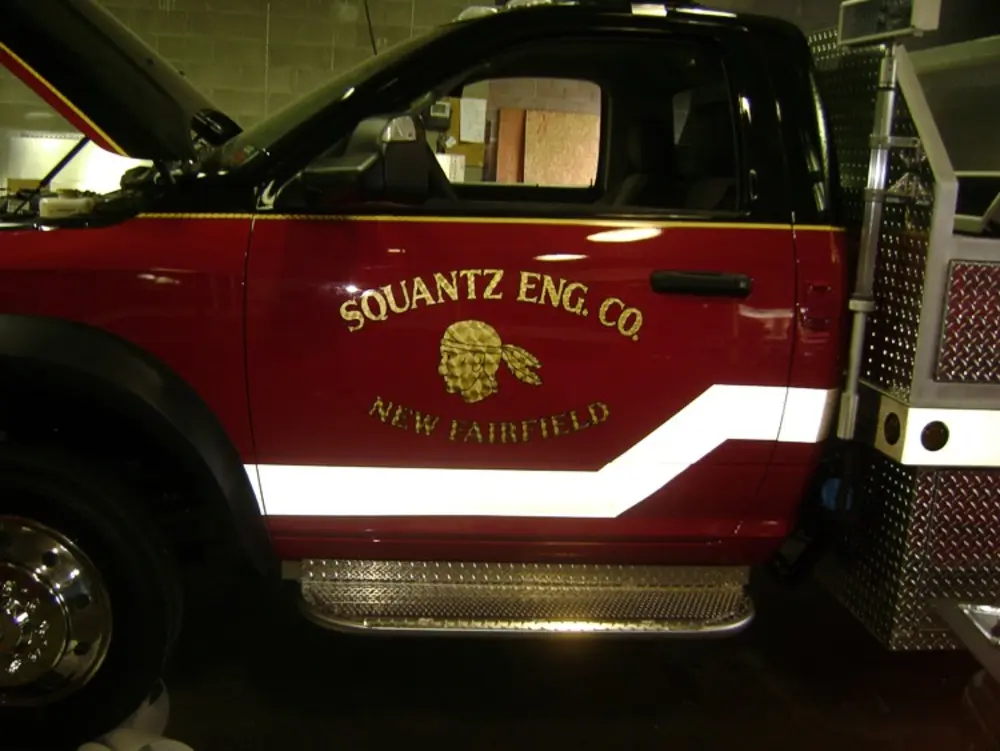 Exterior view of small fire truck showing cab, body compartments, and wheel/tire area.