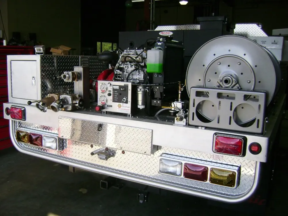 Exterior view of small fire truck showing cab, body compartments, and wheel/tire area.