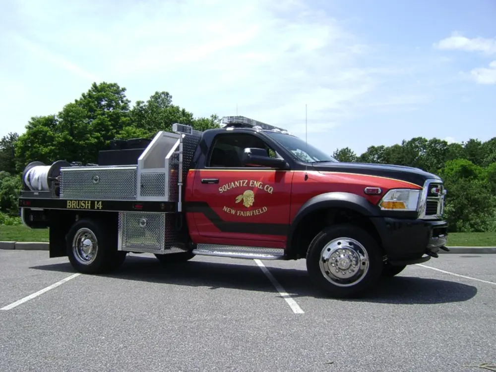 Exterior view of small fire truck showing cab, body compartments, and wheel/tire area.