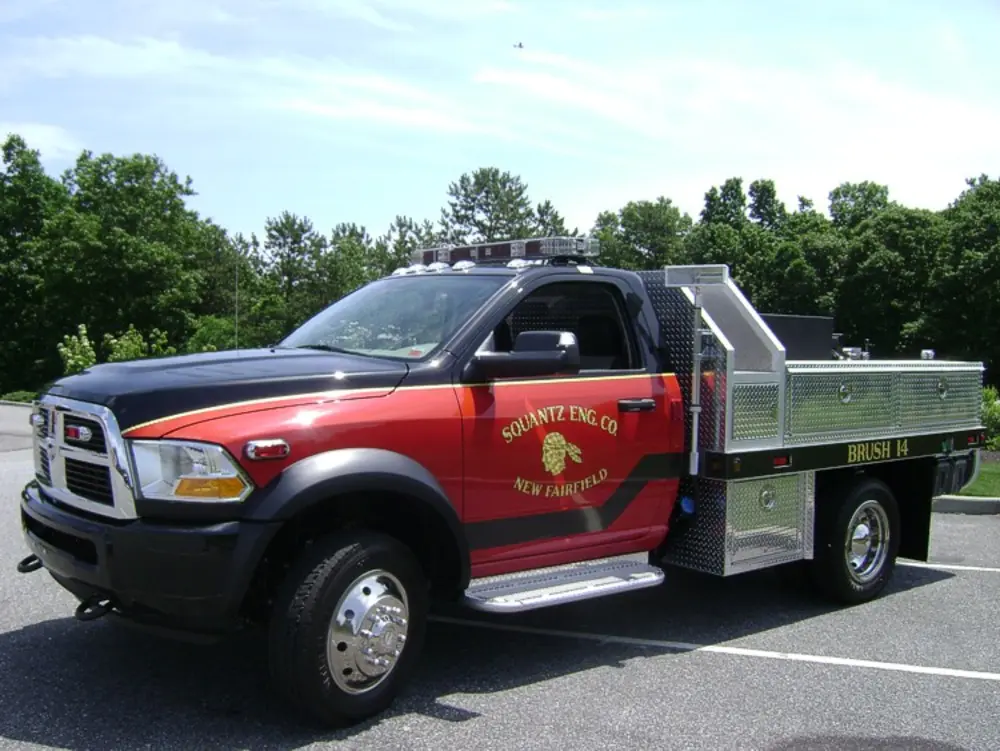 Exterior view of small fire truck showing cab, body compartments, and wheel/tire area.