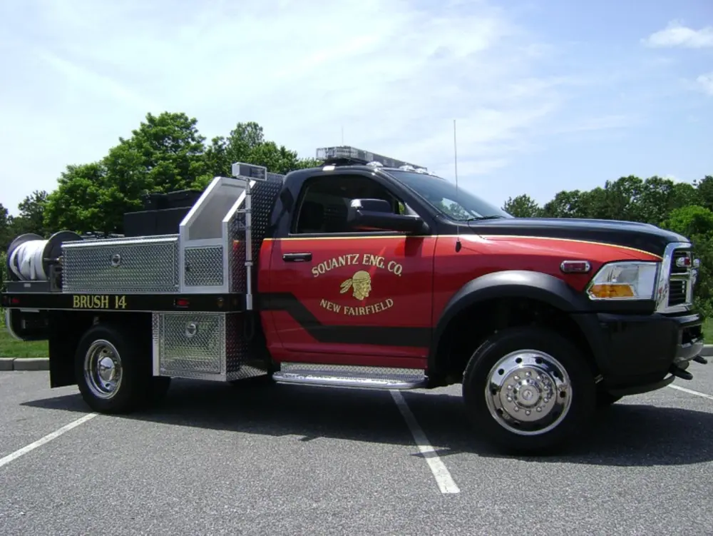 Exterior view of small fire truck showing cab, body compartments, and wheel/tire area.