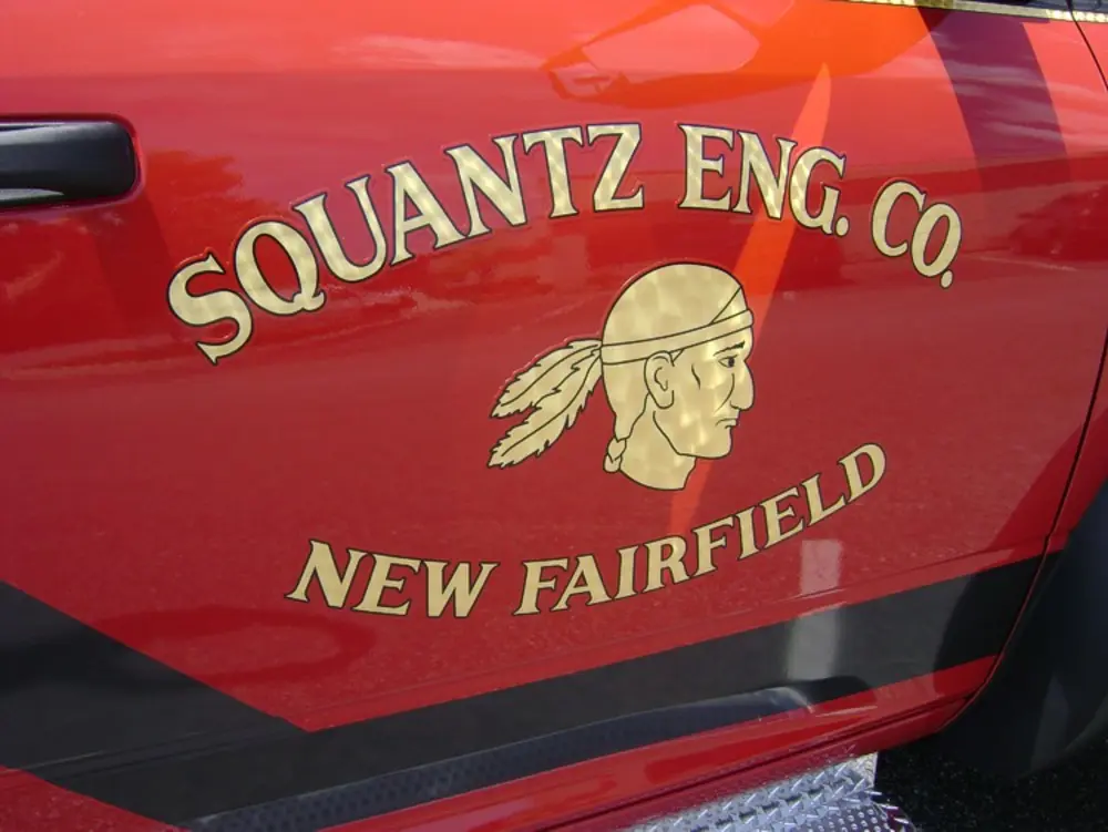 Exterior view of small fire truck showing cab, body compartments, and wheel/tire area.