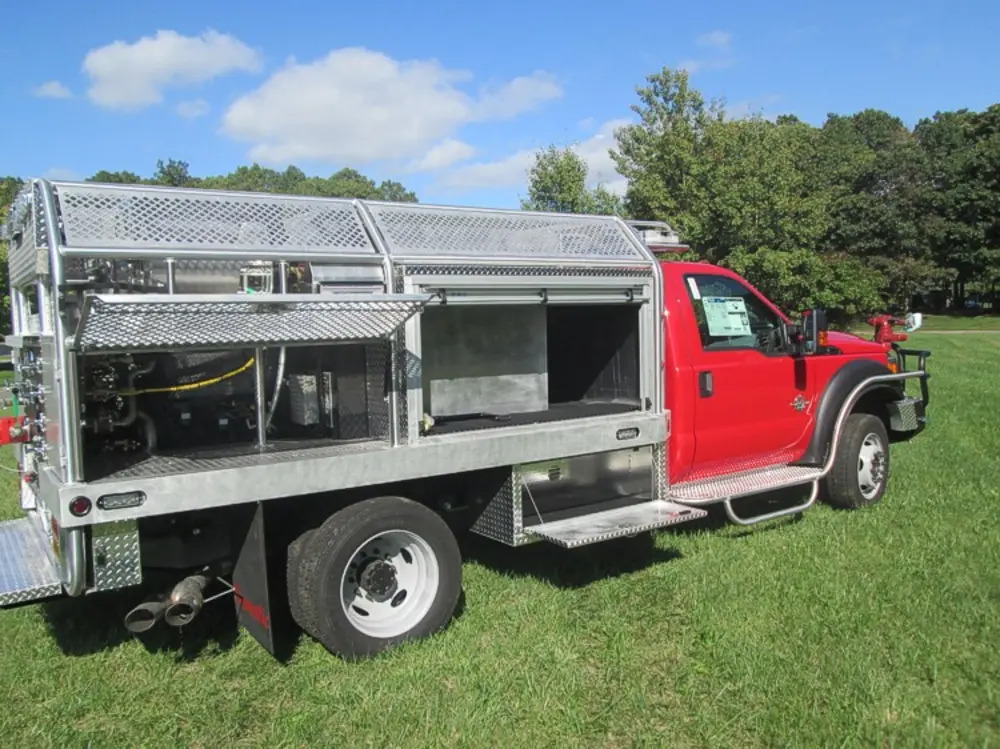 Exterior view of small fire truck showing cab, body compartments, and wheel/tire area.