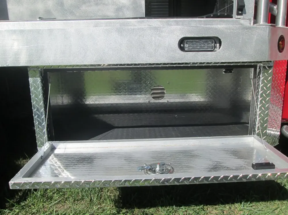 Exterior view of small fire truck showing cab, body compartments, and wheel/tire area.